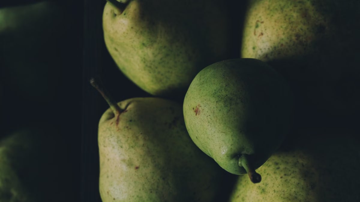 A close-up shot of fresh green pears with a moody lighting effect, highlighting their texture.